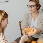 Mother and daughter enjoying a healthy breakfast together with fresh fruits and juice.