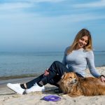 Woman enjoying a sunny day at Kołobrzeg beach with her dog, capturing a perfect seaside moment.