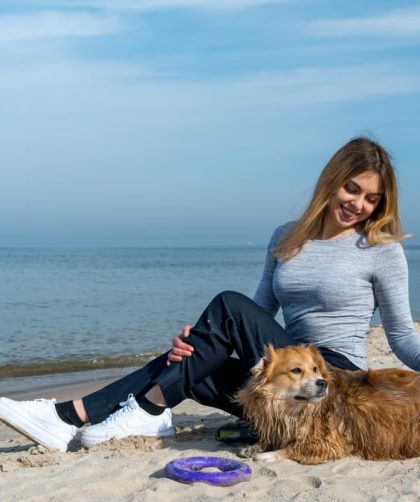 Woman enjoying a sunny day at Kołobrzeg beach with her dog, capturing a perfect seaside moment.