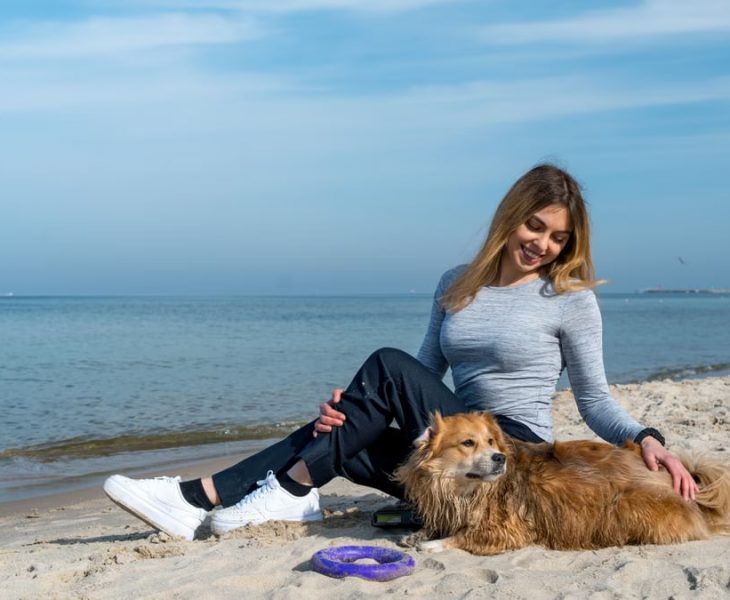 Woman enjoying a sunny day at Kołobrzeg beach with her dog, capturing a perfect seaside moment.