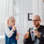 A joyful moment between a father and daughter blowing bubbles indoors, highlighting family fun.
