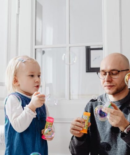 A joyful moment between a father and daughter blowing bubbles indoors, highlighting family fun.